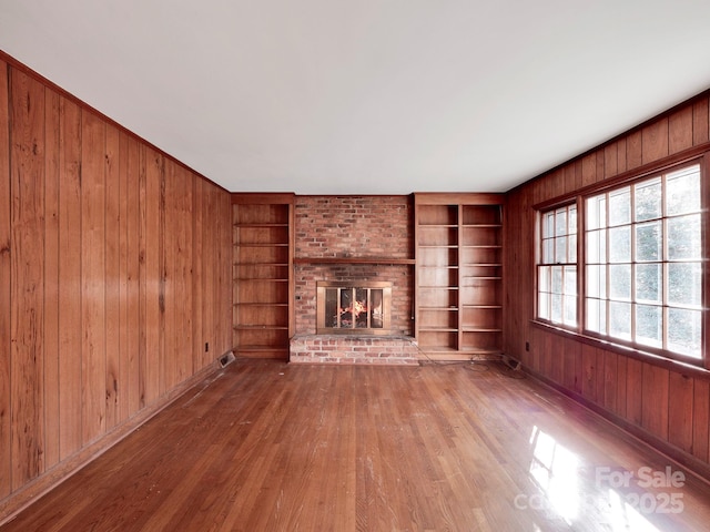 unfurnished living room with wooden walls, built in features, hardwood / wood-style flooring, and a brick fireplace