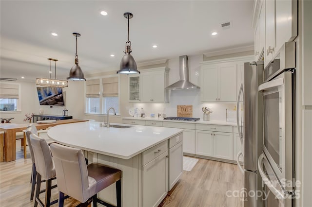 kitchen with sink, a center island with sink, white cabinetry, and wall chimney range hood