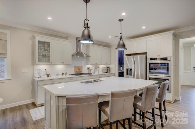 kitchen featuring stainless steel appliances, a center island with sink, white cabinetry, and wall chimney exhaust hood