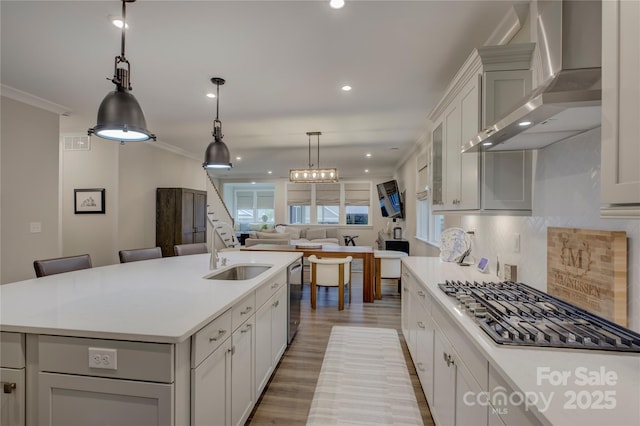 kitchen featuring pendant lighting, a center island with sink, wall chimney range hood, sink, and decorative backsplash