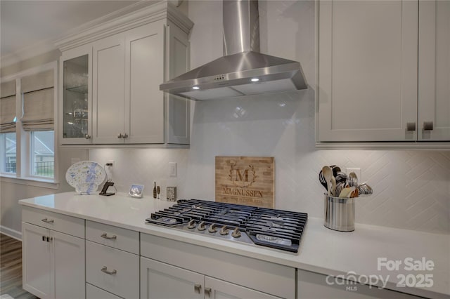 kitchen with tasteful backsplash, white cabinets, wall chimney range hood, and stainless steel gas stovetop