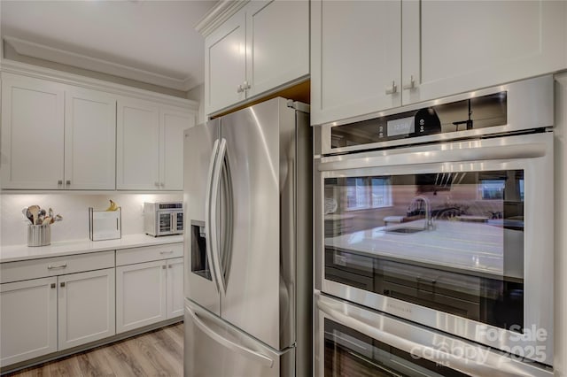 kitchen with white cabinets, crown molding, tasteful backsplash, light hardwood / wood-style floors, and stainless steel appliances