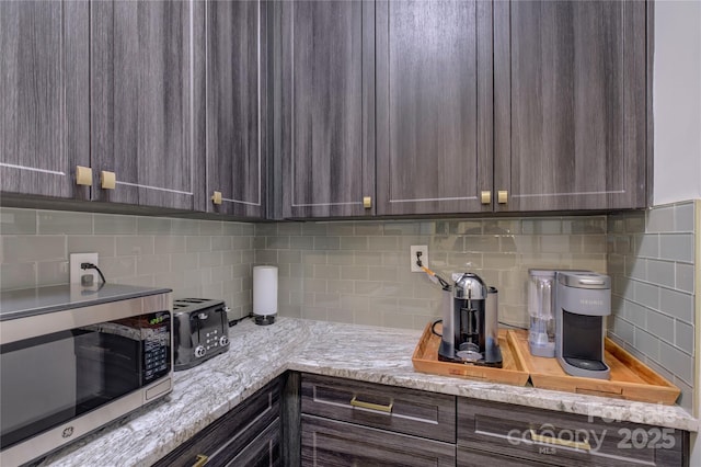 kitchen featuring light stone countertops, dark brown cabinetry, and tasteful backsplash