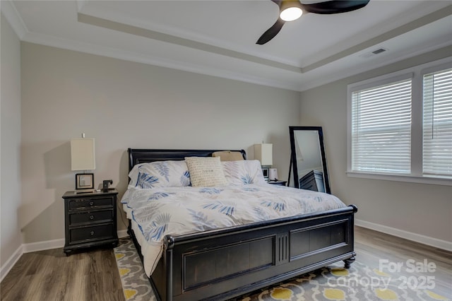 bedroom featuring dark hardwood / wood-style flooring, a raised ceiling, ceiling fan, and crown molding