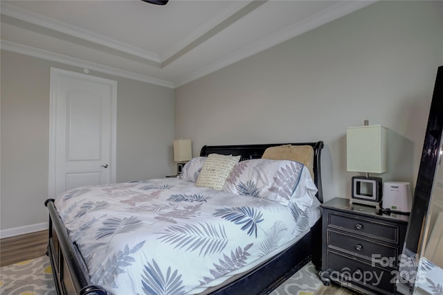 bedroom featuring hardwood / wood-style flooring, a raised ceiling, and ornamental molding