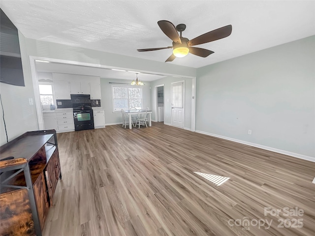 unfurnished living room featuring plenty of natural light, light hardwood / wood-style floors, and ceiling fan with notable chandelier