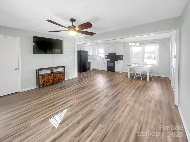 unfurnished living room with sink, light hardwood / wood-style floors, and ceiling fan with notable chandelier