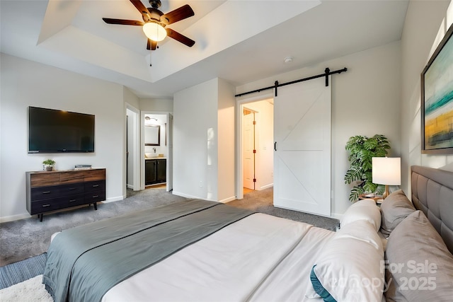 carpeted bedroom featuring a raised ceiling, a barn door, ensuite bathroom, and ceiling fan