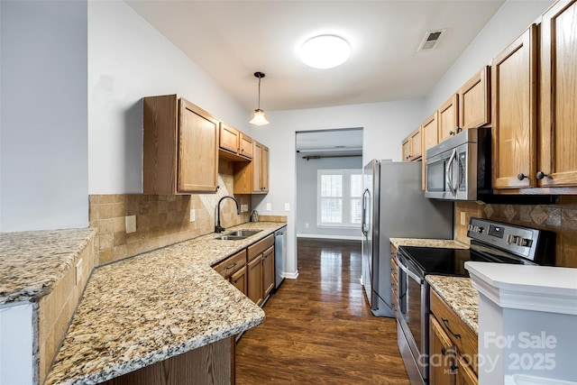 kitchen with backsplash, light stone counters, stainless steel appliances, sink, and hanging light fixtures