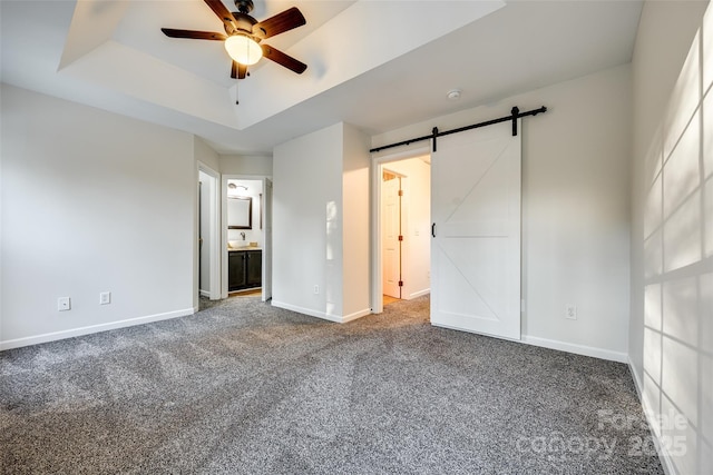 unfurnished bedroom with ensuite bath, ceiling fan, a barn door, carpet floors, and a tray ceiling