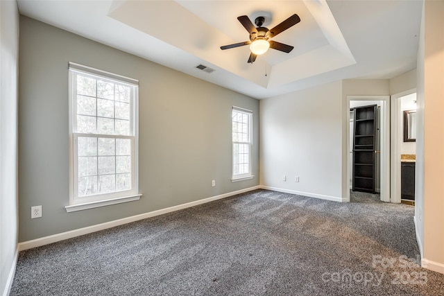 empty room with a raised ceiling, ceiling fan, and dark carpet