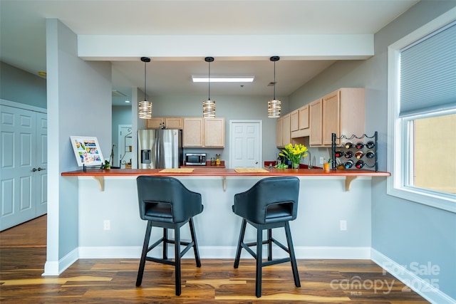 kitchen with stainless steel appliances, light brown cabinets, a kitchen breakfast bar, and decorative light fixtures