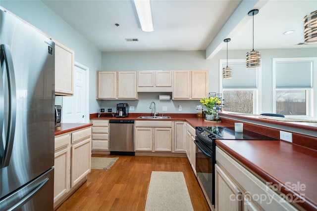 kitchen with appliances with stainless steel finishes, light brown cabinetry, sink, hanging light fixtures, and light wood-type flooring