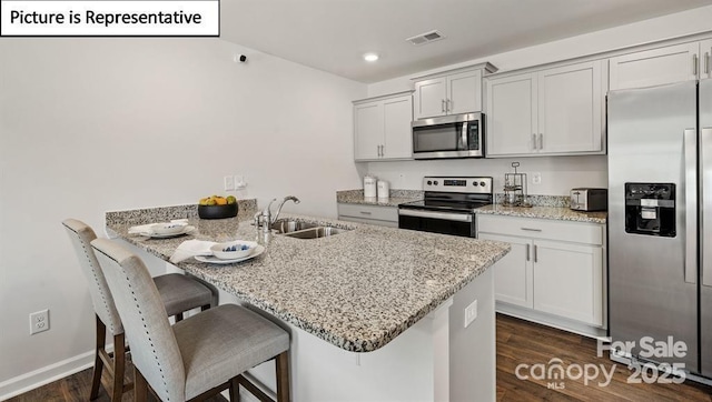 kitchen featuring appliances with stainless steel finishes, light stone counters, a breakfast bar, sink, and white cabinetry