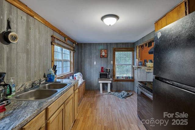 kitchen featuring wooden walls, sink, black appliances, and light hardwood / wood-style floors