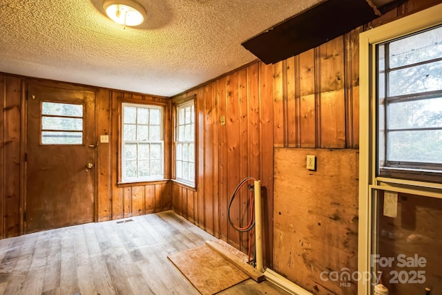 doorway to outside with hardwood / wood-style flooring, a textured ceiling, and wooden walls