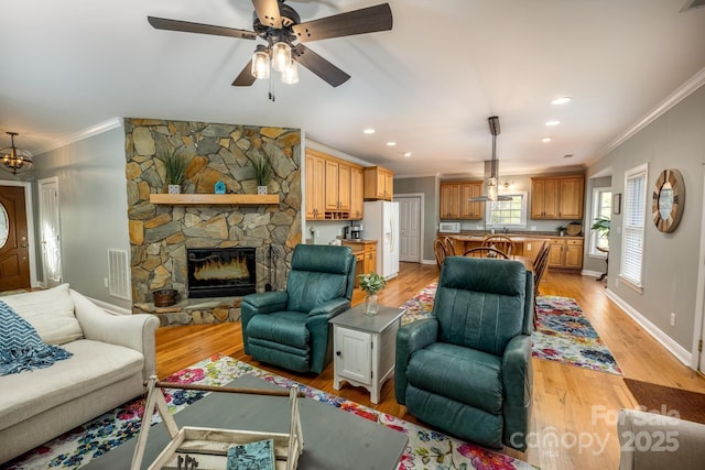 living room with light hardwood / wood-style floors, a stone fireplace, and crown molding