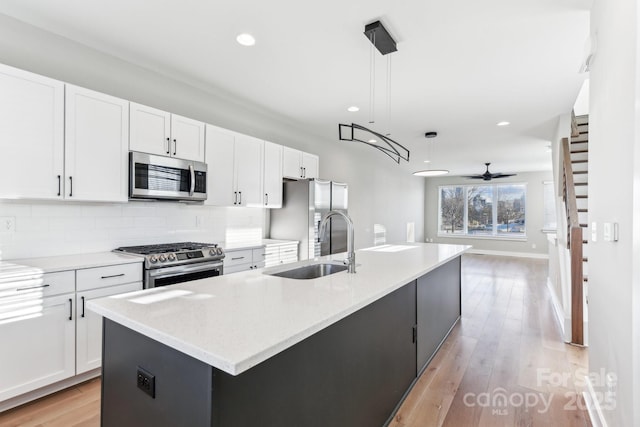 kitchen with stainless steel appliances, a kitchen island with sink, ceiling fan, and hanging light fixtures