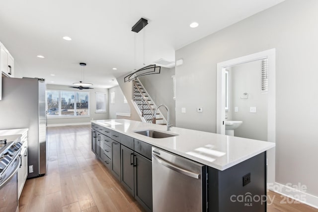 kitchen with decorative light fixtures, an island with sink, appliances with stainless steel finishes, ceiling fan, and sink