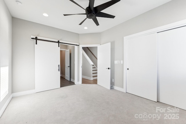 unfurnished bedroom featuring ceiling fan, a closet, a barn door, and carpet flooring