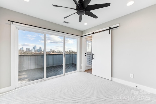 unfurnished room featuring ceiling fan, a barn door, and light colored carpet