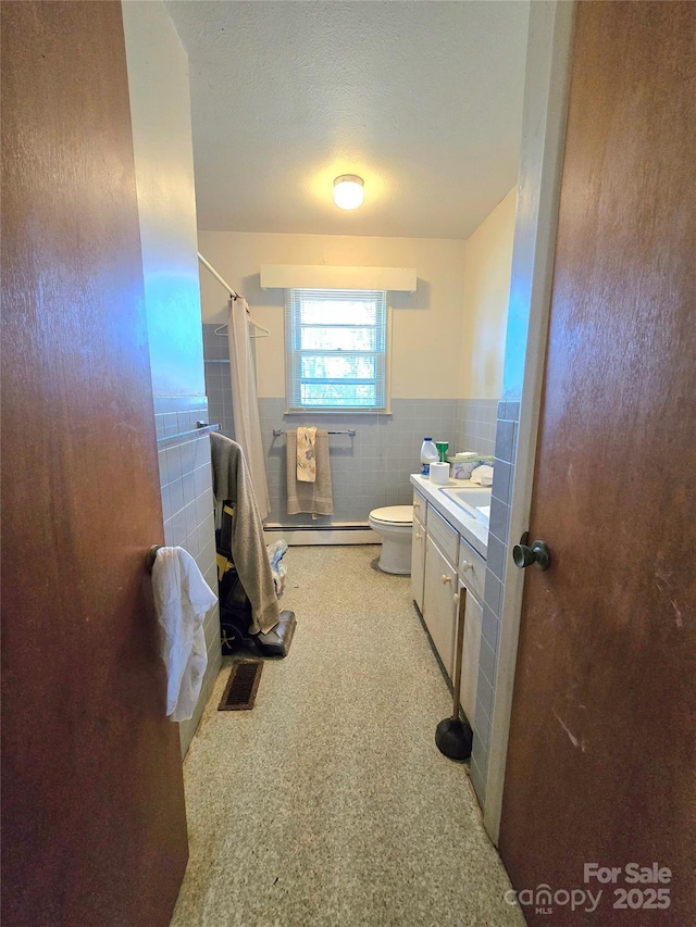 bathroom with curtained shower, baseboard heating, toilet, vanity, and tile walls