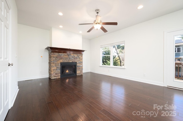 unfurnished living room featuring ceiling fan, dark hardwood / wood-style flooring, and a stone fireplace