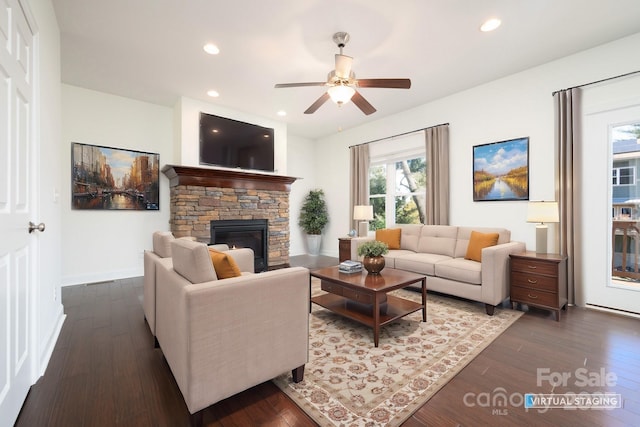 living room featuring ceiling fan, dark hardwood / wood-style floors, and a stone fireplace