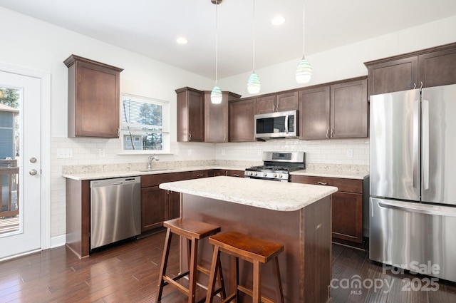 kitchen featuring pendant lighting, appliances with stainless steel finishes, a center island, dark brown cabinetry, and sink