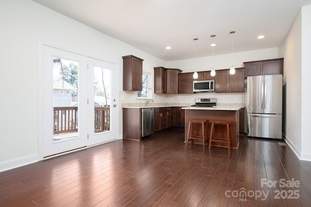 kitchen featuring appliances with stainless steel finishes, dark hardwood / wood-style floors, decorative light fixtures, a kitchen breakfast bar, and a center island