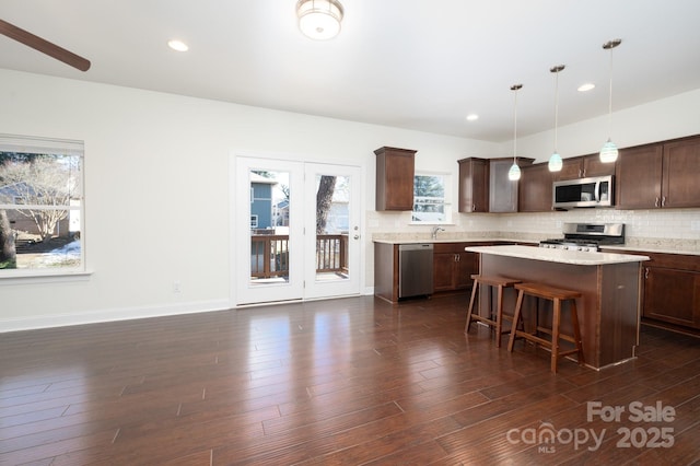 kitchen featuring a kitchen bar, appliances with stainless steel finishes, dark brown cabinets, a kitchen island, and pendant lighting