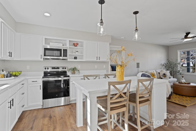 kitchen with appliances with stainless steel finishes, ceiling fan, pendant lighting, white cabinets, and light hardwood / wood-style floors