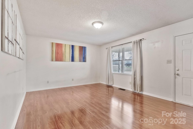 empty room with a textured ceiling, baseboards, and wood finished floors