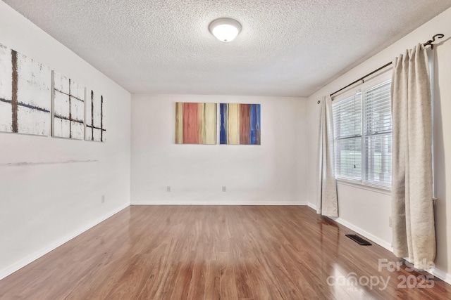 empty room featuring a textured ceiling, wood finished floors, visible vents, and baseboards