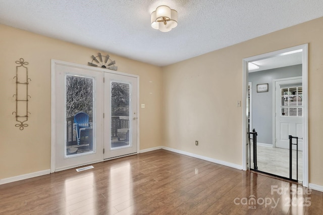 spare room with visible vents, a textured ceiling, baseboards, and wood finished floors