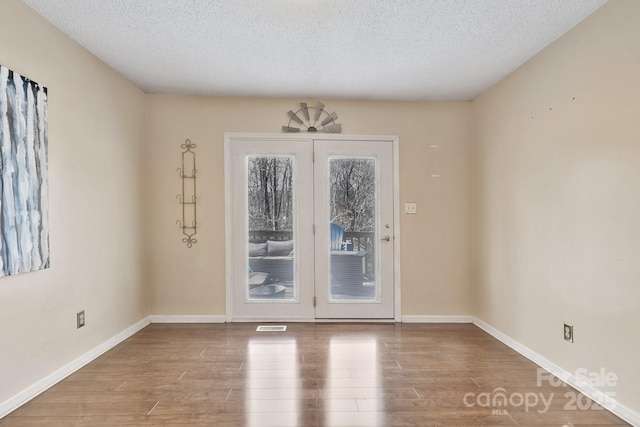 doorway with a textured ceiling, baseboards, and wood finished floors