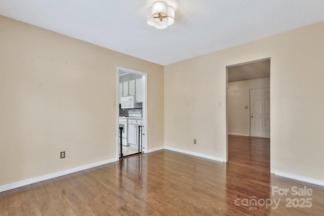 empty room with a textured ceiling, baseboards, and wood finished floors