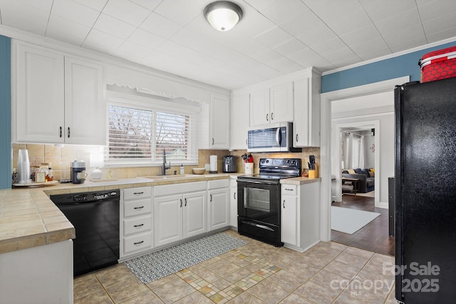 kitchen featuring decorative backsplash, sink, white cabinetry, and black appliances