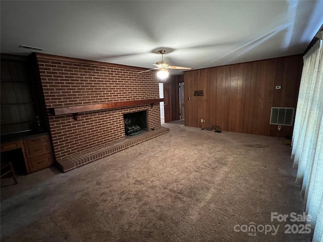 unfurnished living room with wood walls, ceiling fan, a fireplace, carpet floors, and brick wall