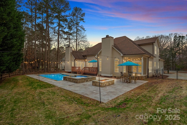 pool at dusk featuring an in ground hot tub, a fire pit, a lawn, and a patio