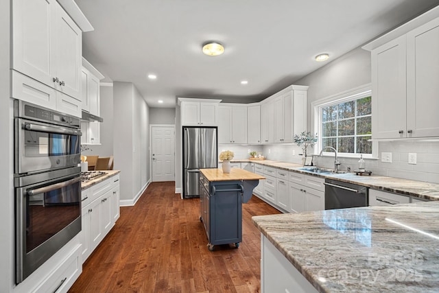 kitchen featuring white cabinetry, butcher block counters, stainless steel appliances, a center island, and sink