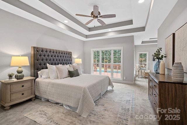 bedroom with ceiling fan, light colored carpet, and a tray ceiling