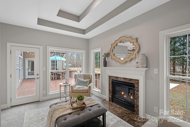 sitting room with a high end fireplace, light colored carpet, and a raised ceiling