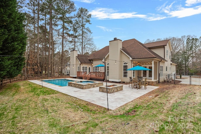 rear view of property featuring a pool with hot tub, a fire pit, a yard, and a patio