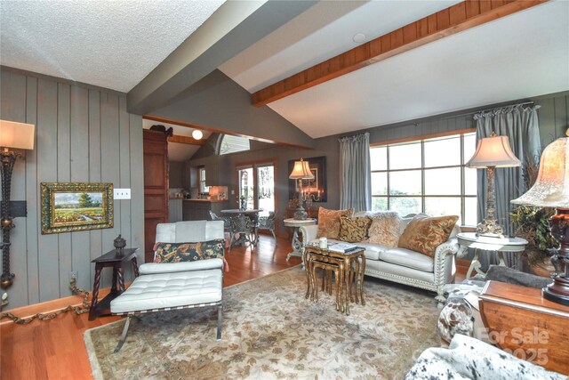 living room with hardwood / wood-style flooring, lofted ceiling with beams, wood walls, and a textured ceiling