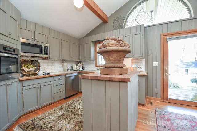 kitchen with light wood-type flooring, stainless steel appliances, vaulted ceiling with beams, butcher block countertops, and a kitchen island