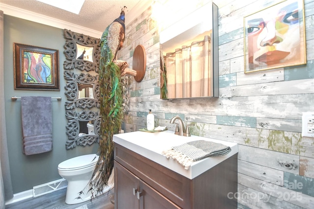 bathroom featuring vanity, wooden walls, toilet, ornamental molding, and a textured ceiling