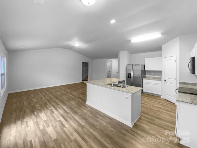 kitchen with appliances with stainless steel finishes, white cabinets, sink, vaulted ceiling, and a center island with sink