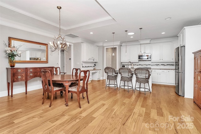 dining area featuring sink, a chandelier, ornamental molding, a tray ceiling, and light hardwood / wood-style floors