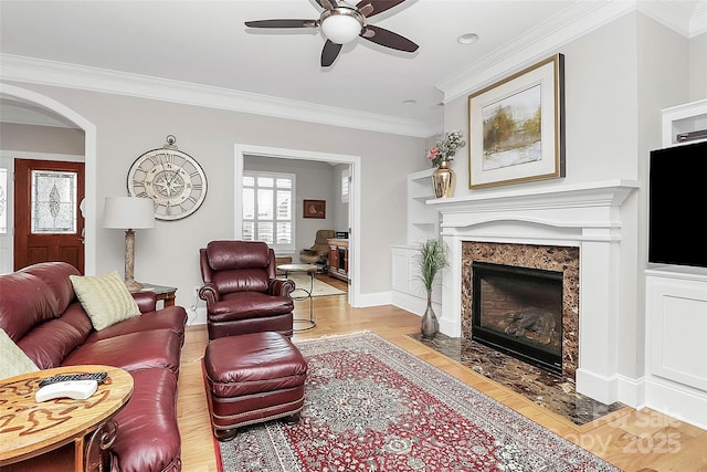 living room with baseboards, arched walkways, a ceiling fan, crown molding, and a fireplace